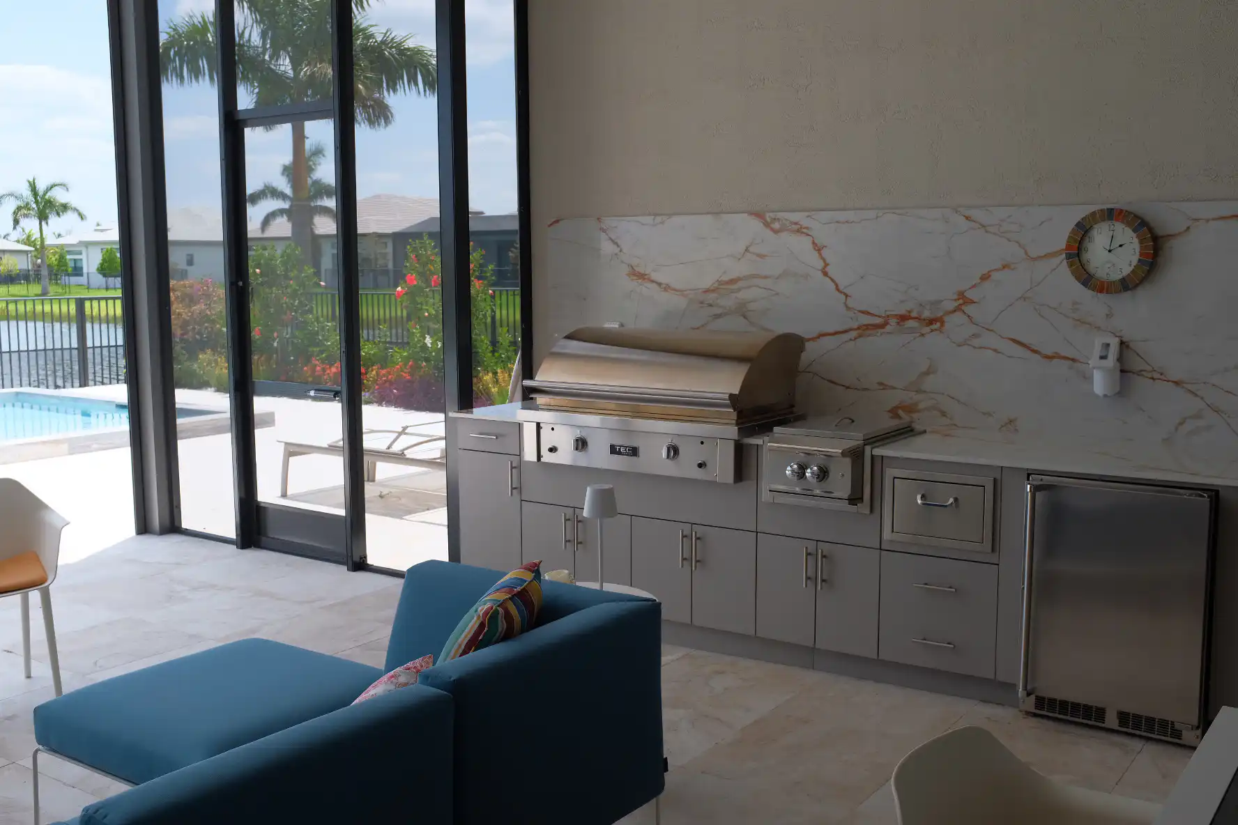 Luxury outdoor kitchen in Boynton Beach Florida with a wide Dekton Awake backsplash, Werever HDPE cabinets in Cashmere Colorway, TEC 44-inch built-in grill, Blaze LUX Power burner, and pool view through patio screen.