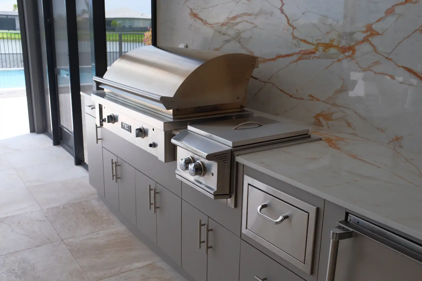TEC 44-inch infrared grill with open lid and Blaze Lux power burner installed in custom outdoor kitchen with Dekton Awake countertops