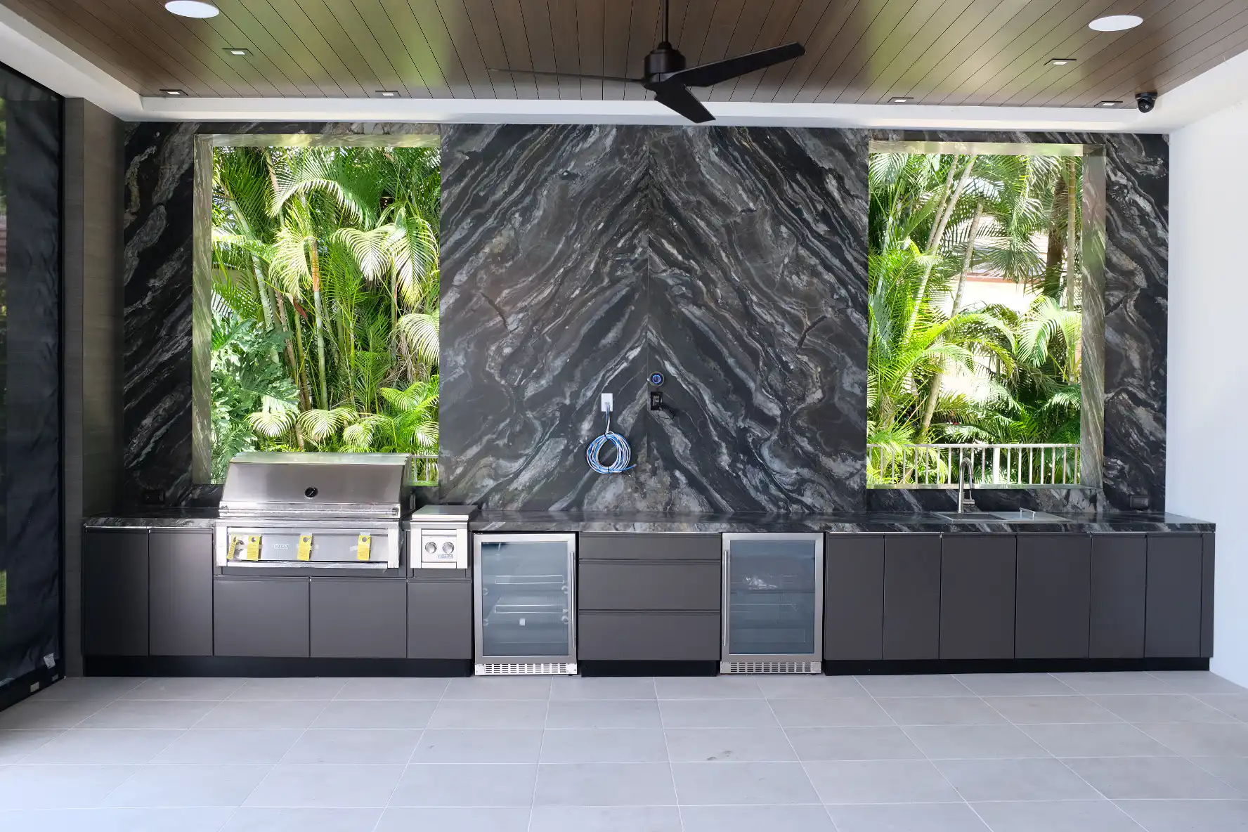 Full view of Delray Beach outdoor kitchen with book-matched Belvedere quartzite wall, dual Azure refrigerators, Lynx Professional grill, Danver bronze cabinets, and Ruvati undermount sink under covered patio